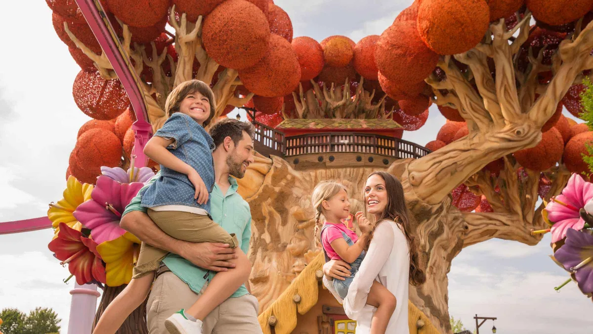 A father lifting his son in front of a giant flower-decorated tree ride at Gardaland Park