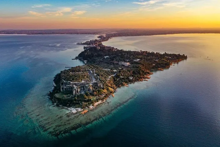 The Sirmione peninsula from the air at sunset, its long tip reaching into an orange and blue lake
