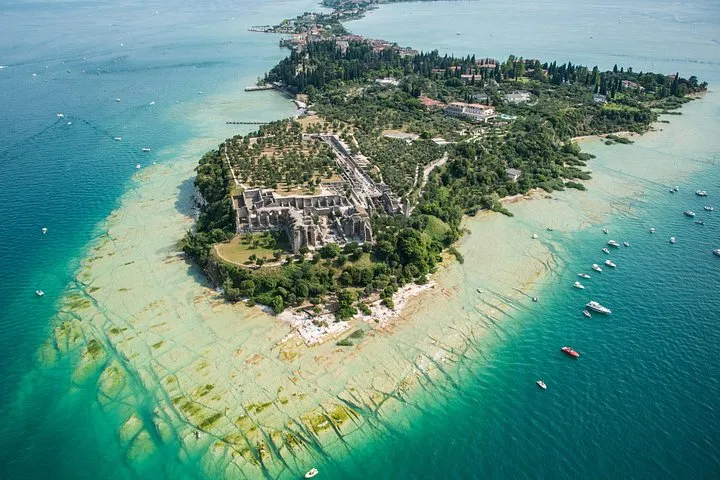 Shallow turquoise shoals and the green northern tip of the Sirmione peninsula seen from high above