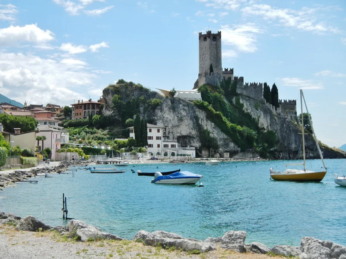 Malcesine castle on its rock above a turquoise bay with moored boats