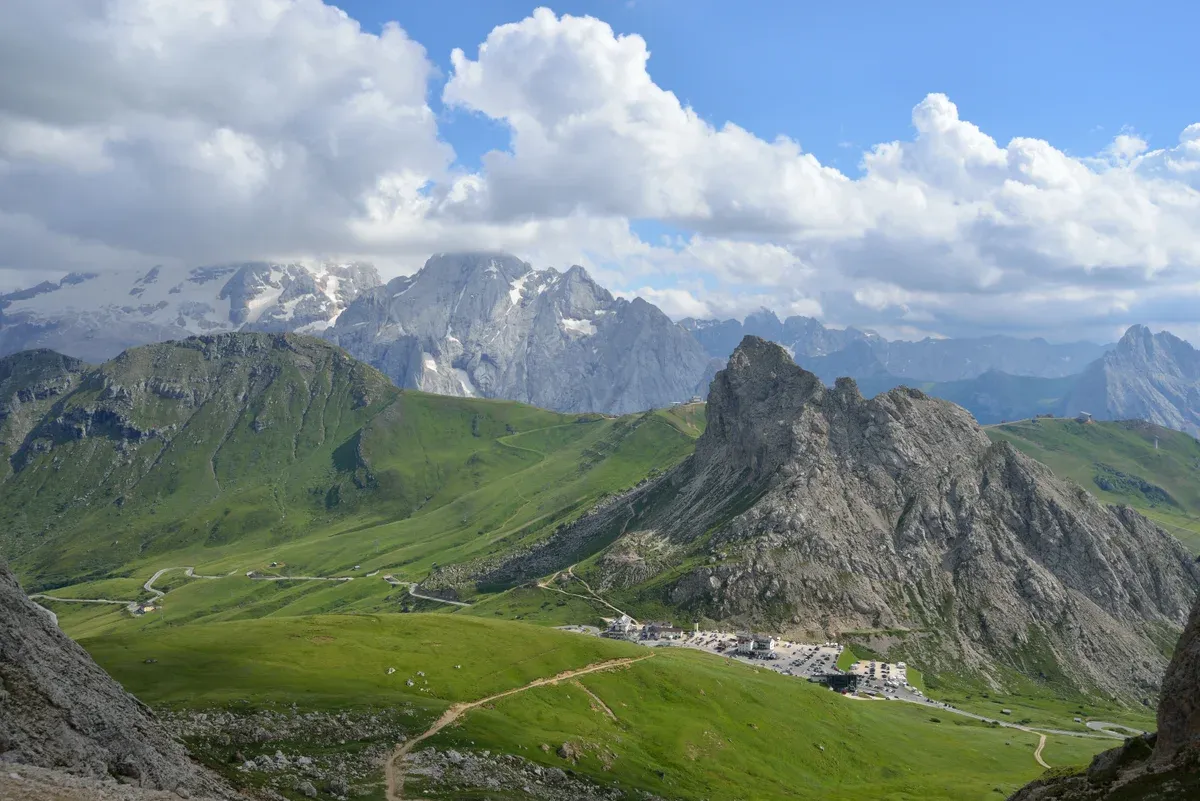 Green meadows and rock peaks at the Pordoi Pass in the Dolomites under summer clouds
